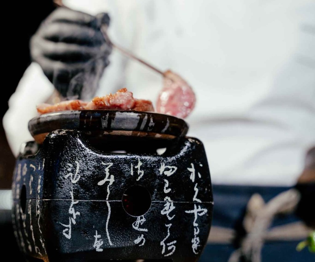 A close up shot of a chef cooking pieces of steak on a stone grill for Yakitori Night