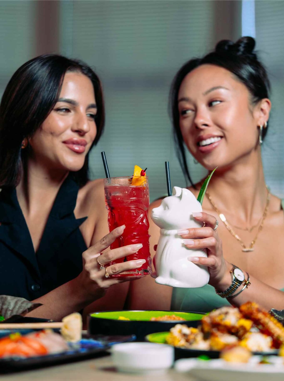 Two female friends sit together clinking their glasses while enjoying Industry Locals Night at Katsuya South Beach