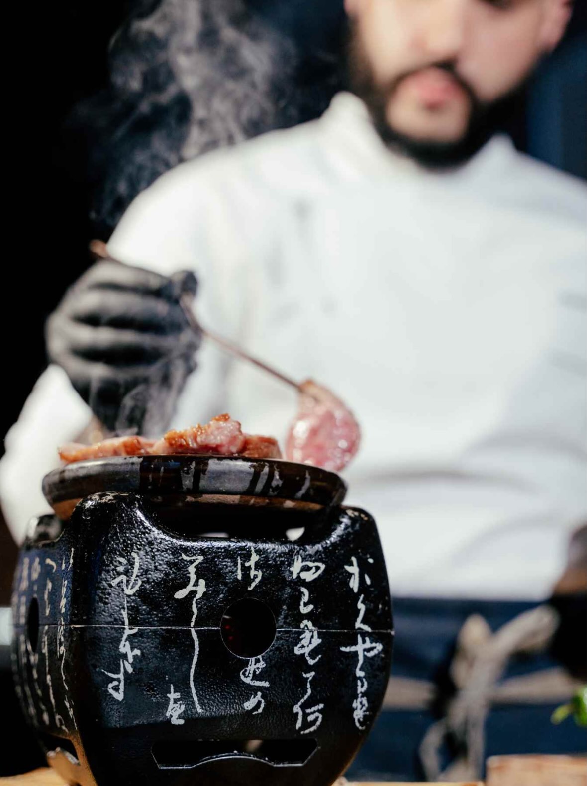 A close up shot of a chef cooking pieces of steak on a stone grill for Yakitori Night