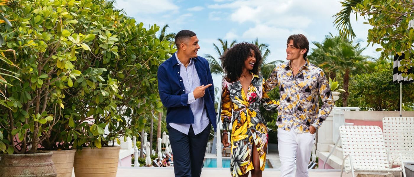 two men and a woman walking outside SLS Baha Mar with a pool in the background, surrounded by beautiful and lush greenery