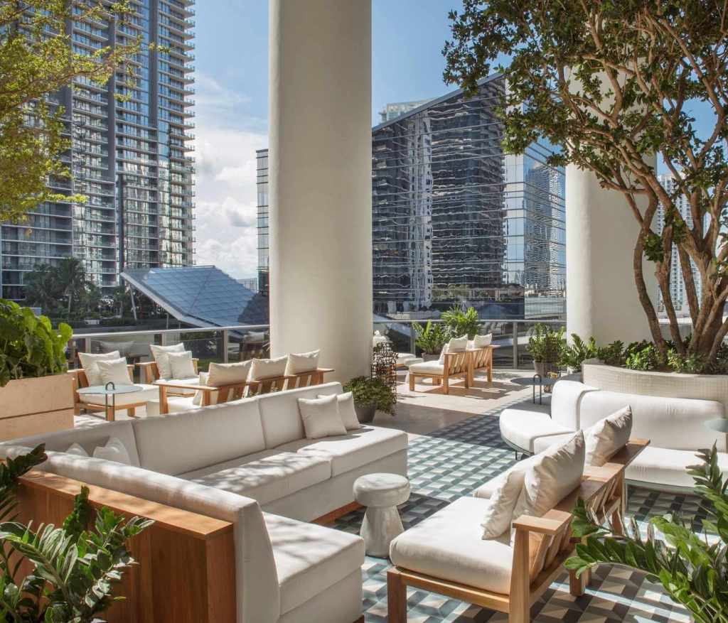 Cadeiras e sofás dispostos no exterior num dia de sol no Rooftop Garden do SLS LUX Brickell