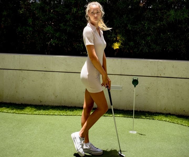 Une mannequin blonde tient un club de golf dans les mains près du parcours de minigolf