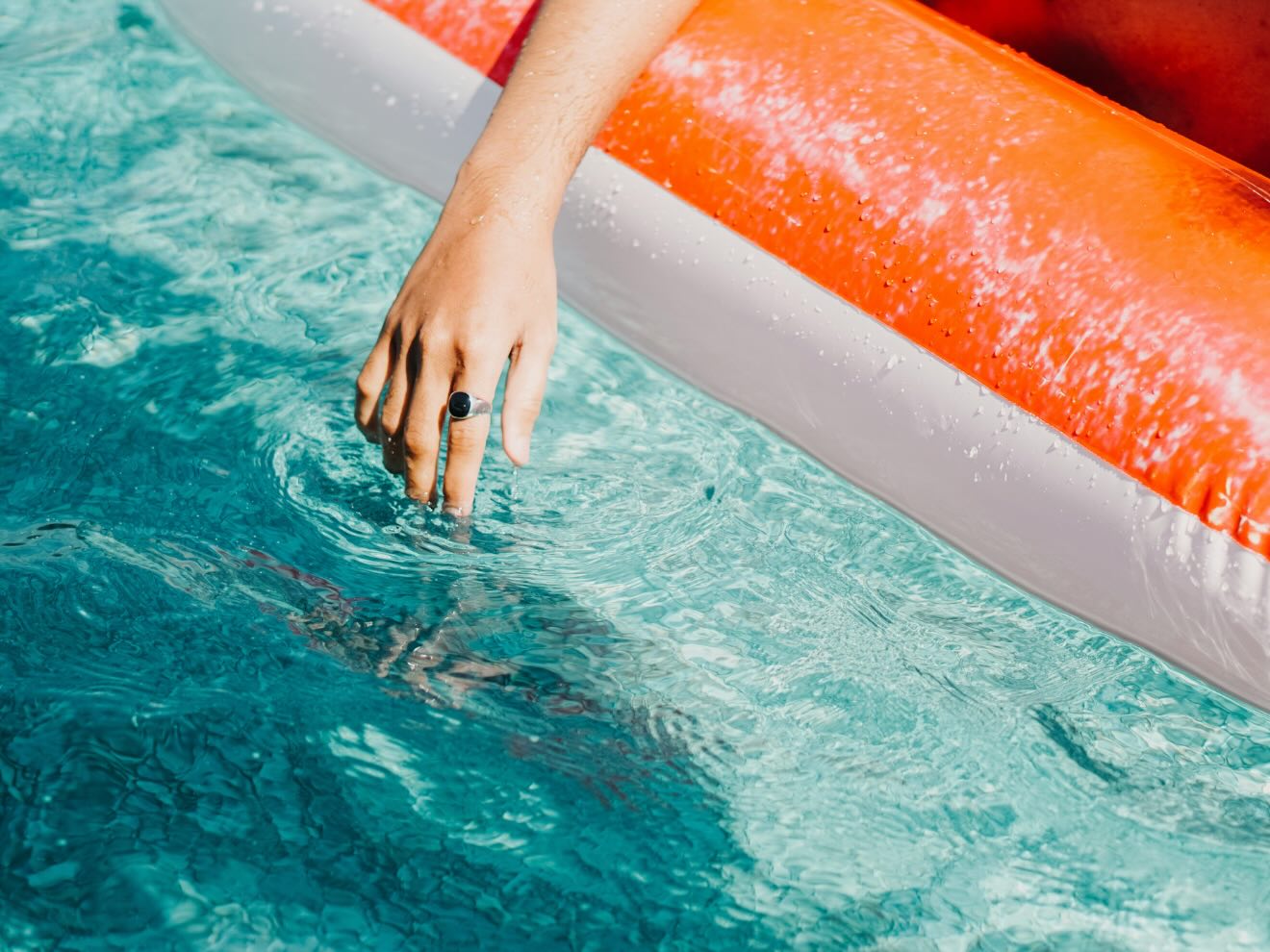 a hand extending from someone unseen on a floatie into a pool