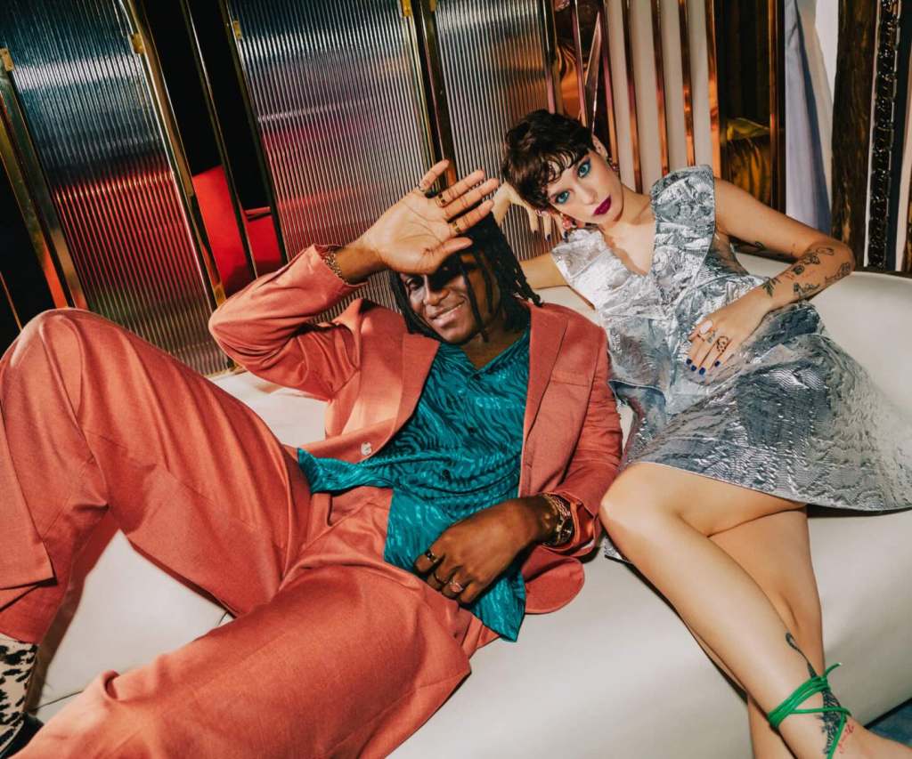 a woman in a bright silver dress sitting next to a man in an orange suit on a white couch