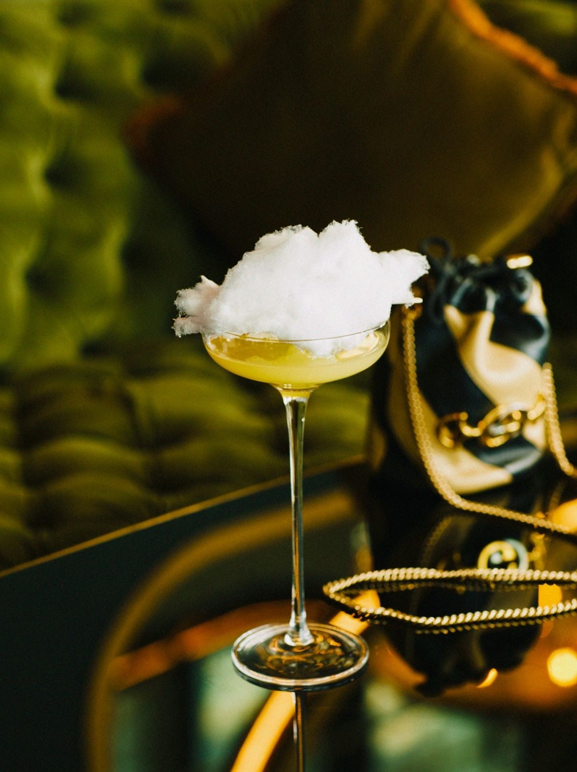 A yellow cocktail sits with a cotton candy cloud garnish