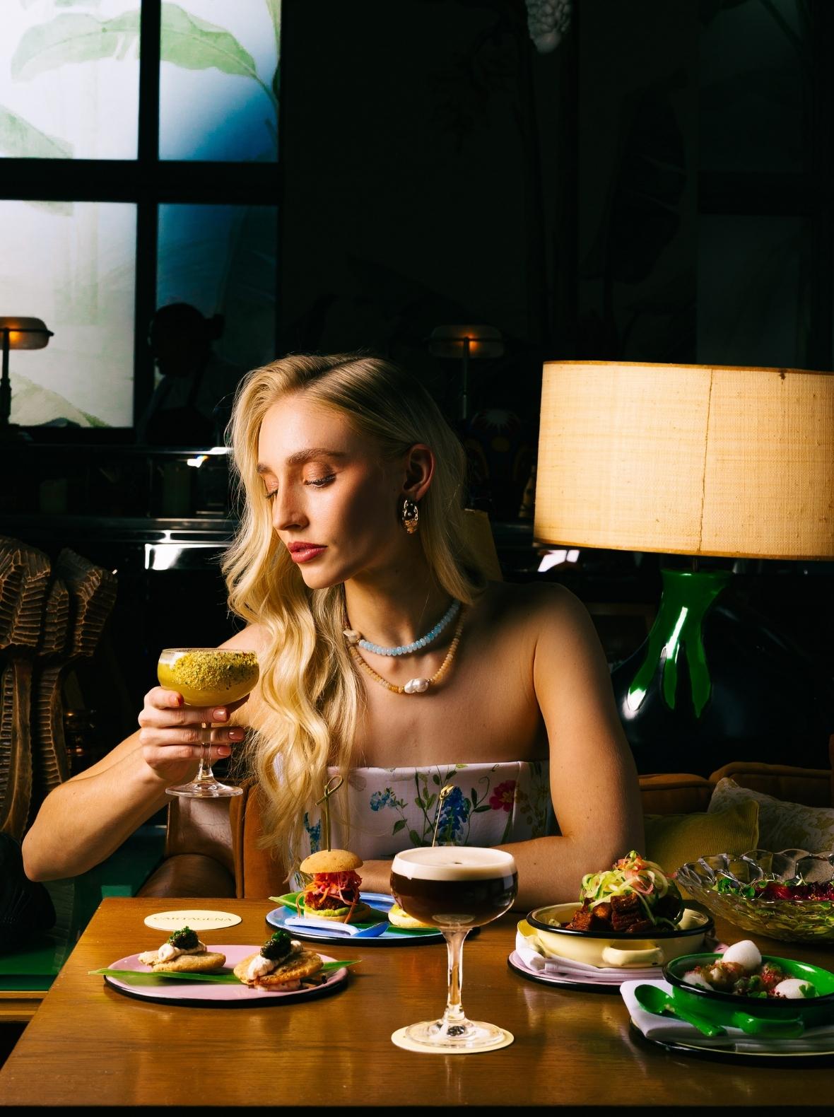 A female model leans forward to sip her drink at Cartagena