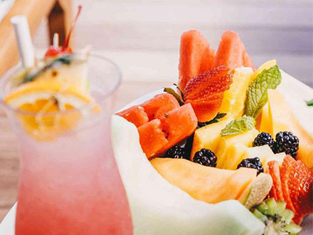 A refreshing fruit salad next to a cup of pink lemonade.