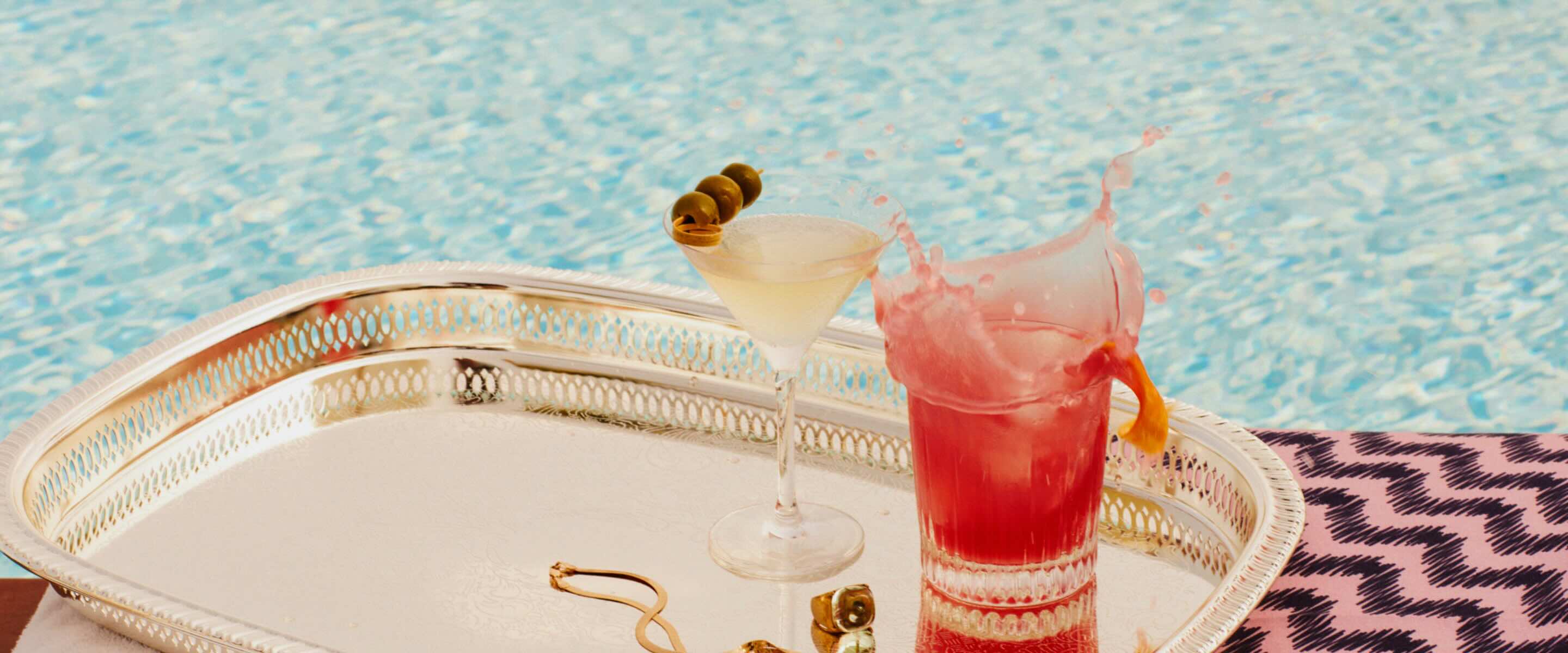 two cocktails on a silver platter by a pool 