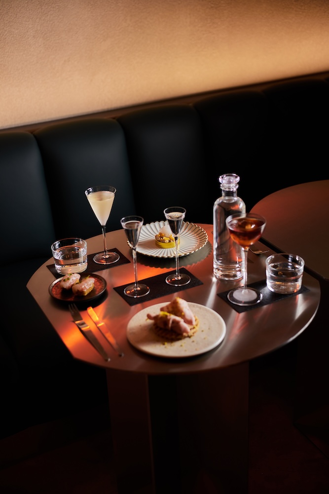 cocktails and elegant small plates of food with soft lighting on a table in a booth