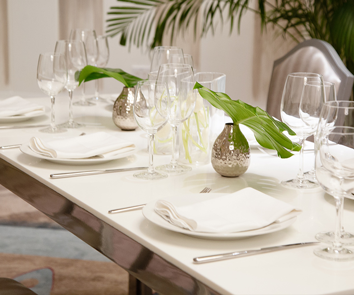 A beautiful table setting with white napkins, places, silverware and silver vases with a leaf.