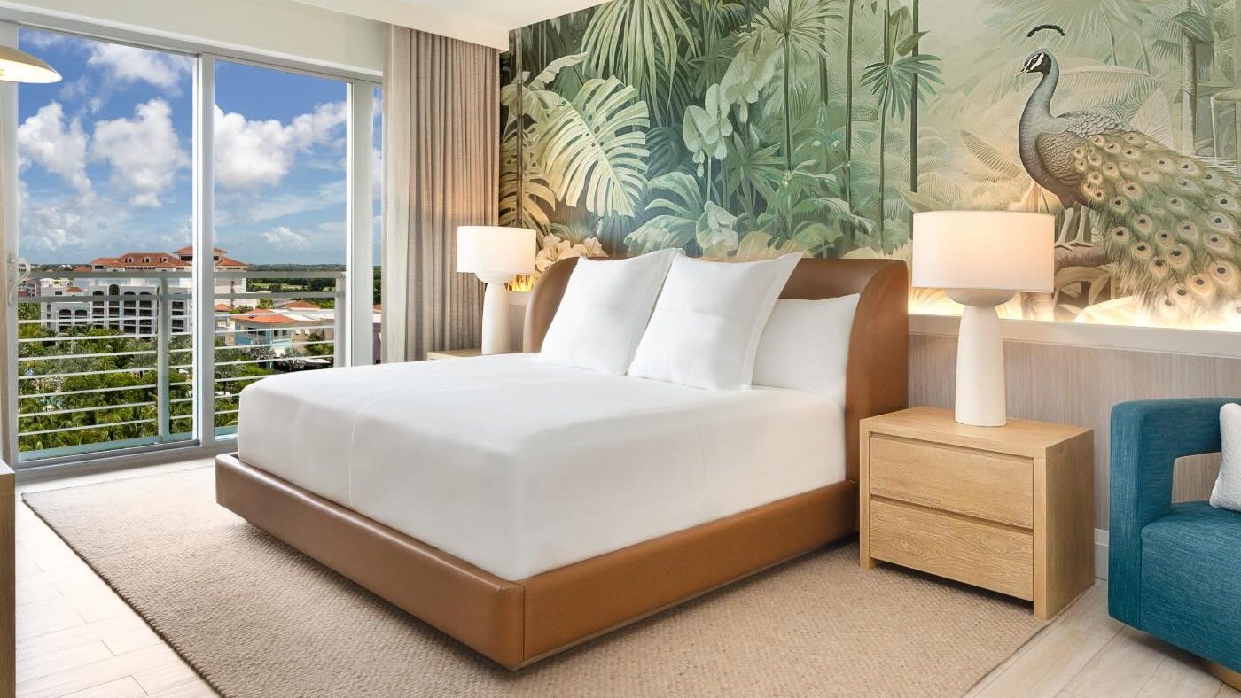 a king bed in a leather bed frame with two bedside tables and tropical wallpaper on the walls