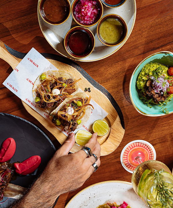 Overhead shot of colorful Mexican food, sauces and drinks with a hand reaching for food