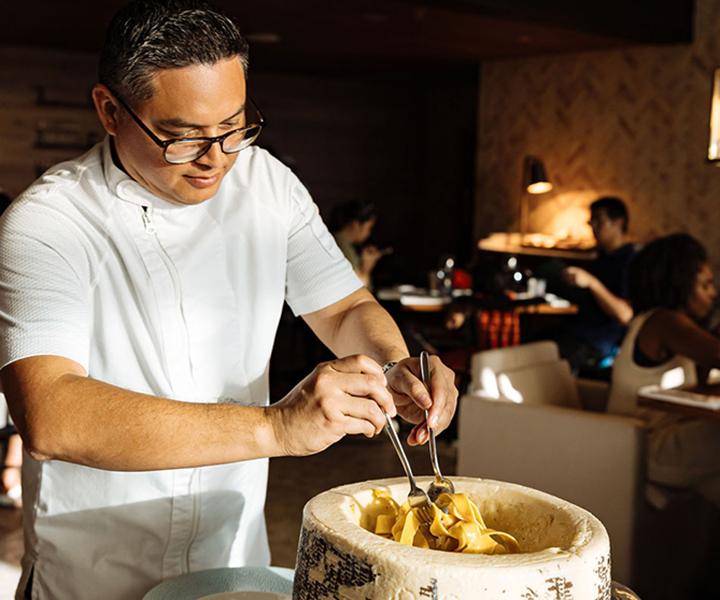 A man tossing pasta in a parmesan bowl