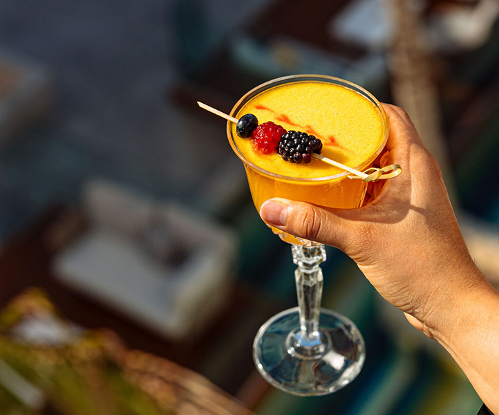 orange yellow cocktail with a fruit garnish in someone's hand 
