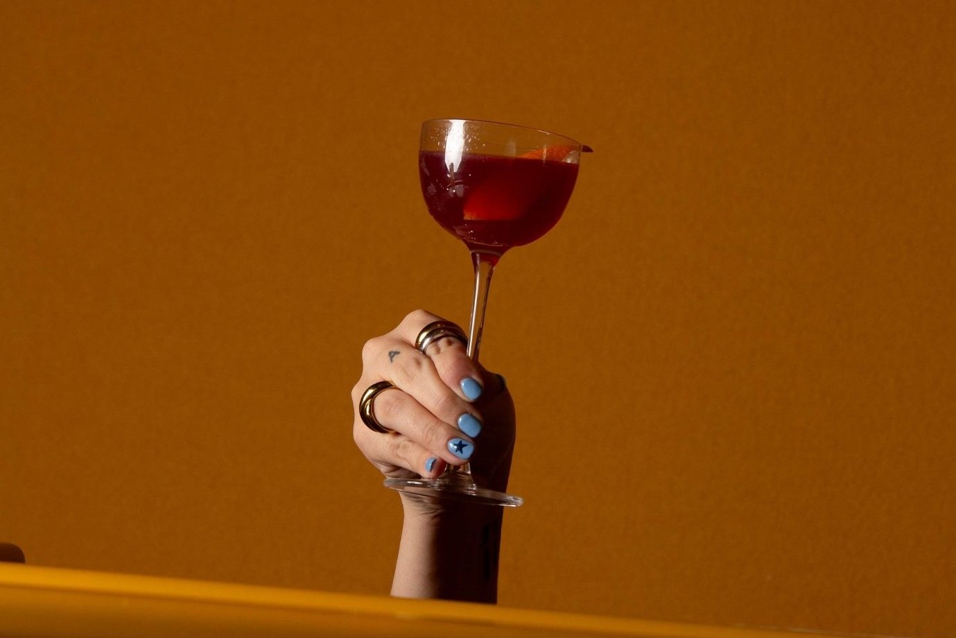 a hand holding a red cocktail on yellow background at lora restaurant at sls barcelona