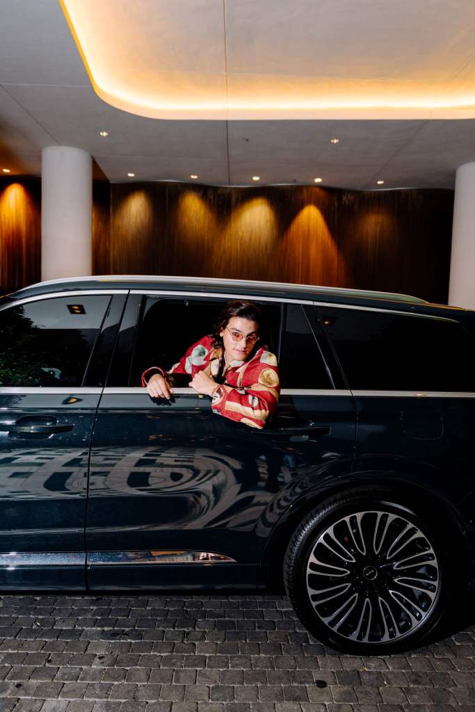 man in stylish outfit looking out from the window of rare seat of black car 